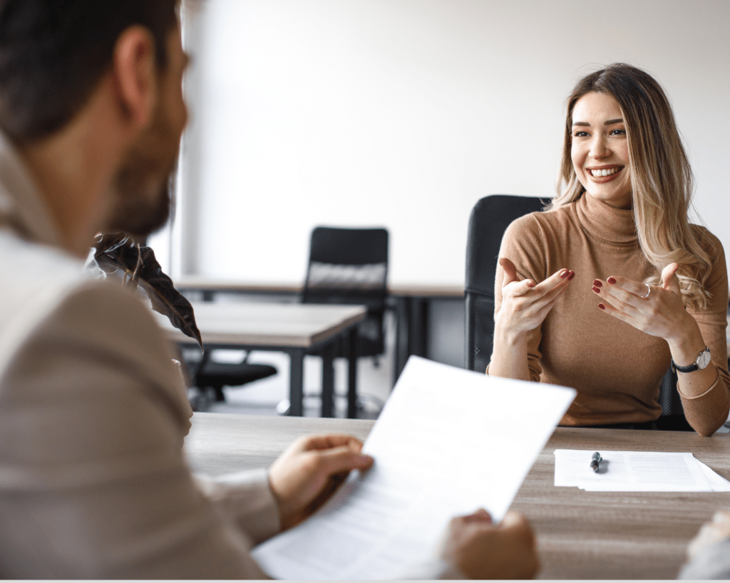 Femme durant un entretient d'embauche assise derrière une table souriant au recruteur en face d'elle.
